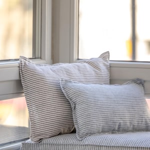May include: A window seat cushion with a gray and white striped pattern. Two pillows are on the cushion, one with a gray and white striped pattern and the other with a white and black striped pattern.
