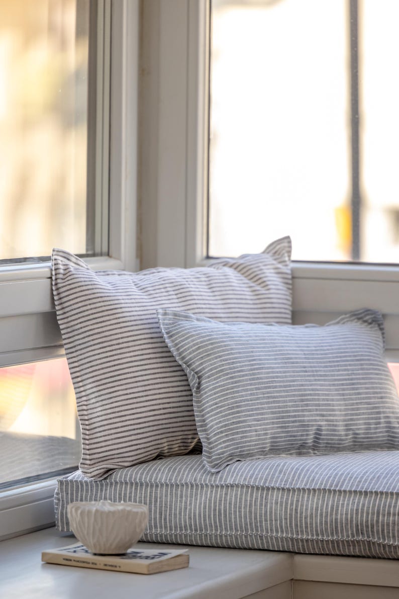 May include: A window seat cushion with a gray and white striped pattern. Two pillows are on the cushion, one with a gray and white striped pattern and the other with a white and black striped pattern.