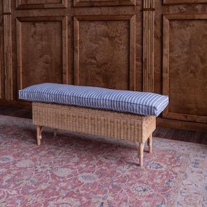 May include: A woven storage bench with a blue and white striped cushion. The bench is sitting on a red patterned rug in front of a wood paneled wall.