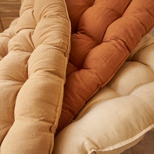 May include: Three tufted cushions in different shades of brown. The cushions are made of a soft, textured fabric and have a slightly rounded shape.