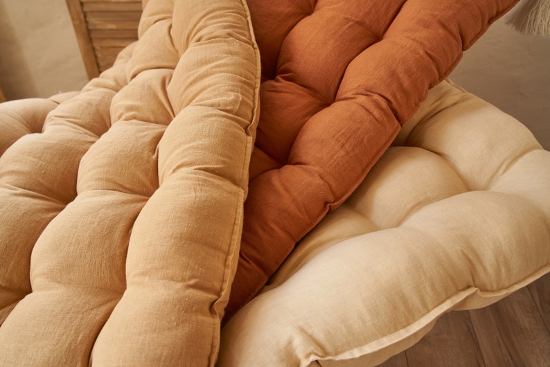 May include: Three tufted cushions in different shades of brown. The cushions are made of a soft, textured fabric and have a slightly rounded shape.