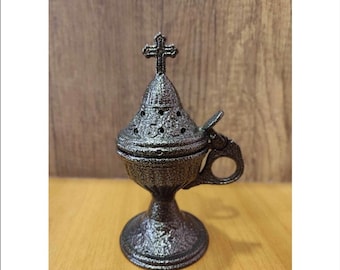 May include: A silver metal incense burner with a cross on top and a handle. The burner has a textured surface and a round base.