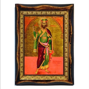 Puede incluir: Icono de una figura religiosa enmarcado en tonos dorados. La figura viste una túnica verde y roja, sosteniendo una cruz. El fondo es dorado con un diseño de arco. El marco es marrón oscuro con un borde de pan de oro.