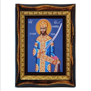 Op de afbeelding: Een religieuze icoon in een lijst met een figuur in blauwe gewaden die een zwaard vasthoudt. De icoon heeft een gouden halo en een blauwe achtergrond. De lijst is donkerbruin met gouden accenten en een decoratieve rand.