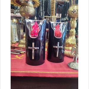 Puede incluir: Dos candelabros negros con una cruz plateada y un diseño de llama roja. Los candelabros están sobre un mantel rojo.