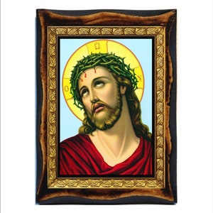 Può includere: Un'icona religiosa incorniciata che raffigura Gesù Cristo con una corona di spine. L'icona ha uno sfondo blu con un'aureola gialla intorno alla testa di Gesù. L'aureola ha le lettere greche Omega e Alpha. L'icona è incorniciata in una cornice di legno scuro con un bordo in foglia d'oro.