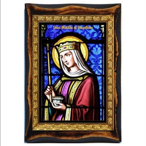 Puede incluir: Una imagen de vitral de Santa Matilde de Ringelheim, una reina que lleva una corona y sostiene un bastón y un cáliz. La imagen está enmarcada en un marco de madera oscura con un borde de hoja de oro.