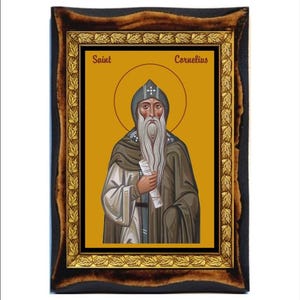 Op de afbeelding: Een ingelijst icoon van Sint Cornelius, een religieuze figuur met een lange witte baard en een gouden halo. Het icoon is geschilderd in een traditionele stijl met levendige kleuren en ingewikkelde details. De lijst is gemaakt van donker hout met gouden accenten.