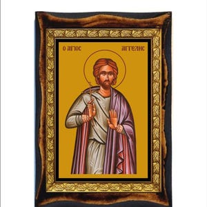以下が含まれることがあります： 黄色い背景に十字架を持った聖人を描いた、額縁に入った宗教的なアイコン。アイコンの上部にはギリシャ語で「O agios aggelos」と書かれている。