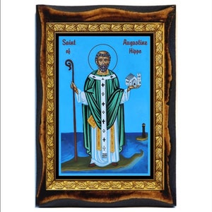 Op de afbeelding: Een ingelijst icoon van Sint Augustinus van Hippo. Het icoon toont een man in een groene robe en een witte soutane die een staf en een kleine kerk vasthoudt. De achtergrond is een blauwe lucht met een waterpartij en een vuurtoren.