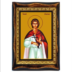 Può includere: Icona religiosa incorniciata raffigurante una figura con un'aureola, che indossa un mantello rosso e una veste bianca, con una croce nera. L'icona è posta su uno sfondo dorato, con le parole "Saint Laurus" sopra. La cornice è marrone scuro con dettagli dorati.