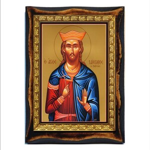 Puede incluir: Icono de una figura religiosa en un marco de madera. La figura lleva una corona, túnicas rojas y azules y sostiene una cruz. El marco tiene un acabado marrón oscuro con detalles de pan de oro. El fondo es dorado con texto griego.
