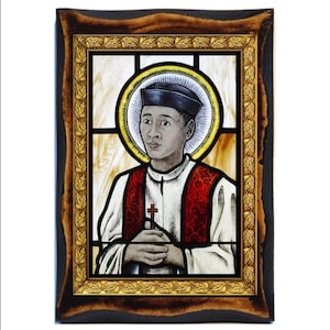 Peut inclure: Vitrail représentant un homme portant un chapeau noir et une chasuble rouge, tenant une croix. L'œuvre est encadrée dans un cadre en bois foncé avec une bordure intérieure dorée. Le fond est de couleur jaune clair.