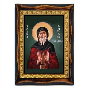 May include: A framed icon of Saint Anthony the Great. The icon is painted in a traditional style with a green background and gold accents. The saint is depicted with a white beard and a red robe.