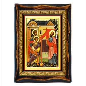 Pode incluir: Um ícone emoldurado que retrata uma cena religiosa com quatro figuras. As figuras são pintadas em um estilo tradicional com cores vibrantes, incluindo vermelho, azul e dourado. O ícone está situado em um fundo amarelo e emoldurado em uma moldura de madeira escura com detalhes dourados.