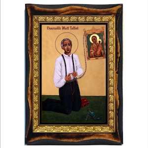 May include: An icon of Venerable Matt Talbot, kneeling with chains, a halo, and a rosary. The image is framed in a dark wood frame with gold accents. A smaller icon of the Virgin Mary and Child hangs on the wall. The text "Venerable Matt Talbot" is at the top.