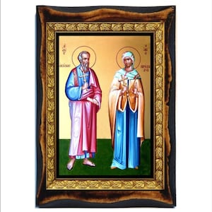 May include: A framed icon depicting two figures, a man and a woman, with halos. The man is wearing a red and white robe and holding a cross. The woman is wearing a blue robe and also holding a cross. The icon is set against a gold background and has a dark wood frame.