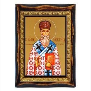 May include: An icon of a religious figure, framed in dark wood with a gold inner border. The figure has a white beard, a crown, and holds a red book. The background is gold, and the figure is wearing a white robe with red and blue accents.