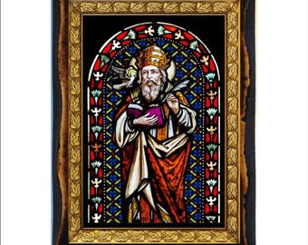 Può includere: Un'opera d'arte in vetro colorato incorniciata raffigurante una figura religiosa con un libro e una penna. La figura indossa abiti ornati, sullo sfondo di una vetrata colorata. La cornice è marrone scuro con un bordo interno dorato.