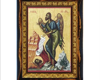 May include: A framed religious icon featuring a figure with wings, holding a scroll. The figure is depicted in green and blue robes, standing on a rocky landscape. The icon is set within a gold and brown ornate frame.