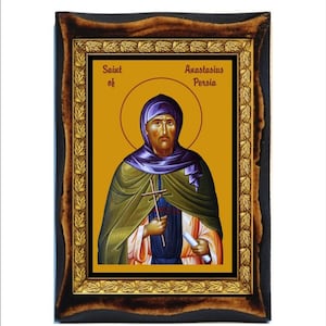 May include: A framed icon of Saint Anastasius of Persia. The icon is painted in a traditional style with a gold background and a detailed depiction of the saint. The frame is made of wood with a dark brown finish and gold accents.