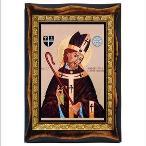 Op de afbeelding: Een ingelijst icoon van Sint Augustinus van Canterbury, een religieuze figuur afgebeeld in een zwarte en rode robe met een gouden rand. Het icoon is geplaatst op een beige achtergrond met een gouden bladgouden lijst.