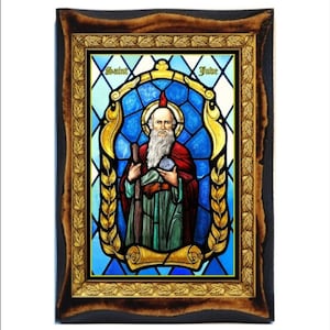 Op de afbeelding: Een afbeelding van Sint Judas Thaddeus in een gebrandschilderd raam. De afbeelding is geplaatst tegen een blauwe achtergrond met gouden accenten. De heilige is afgebeeld met een witte baard en een rode mantel. De lijst is van hout met een donkerbruine afwerking.
