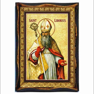 Puede incluir: Icono religioso enmarcado que representa a San Liborio. La imagen muestra a un hombre barbudo con vestiduras religiosas, sosteniendo un báculo y un pequeño objeto. El texto "SAINT LIBORIUS" aparece arriba. El marco es oscuro con detalles dorados.
