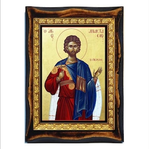 May include: A framed icon of a saint with a gold background. The saint is wearing a red robe with a blue cloak and a gold crown. The icon is surrounded by a gold frame with a brown wooden outer frame. The text on the icon reads "O π.  Θεοδωρος" and "Ο ΠΕΡΣΗΣ".