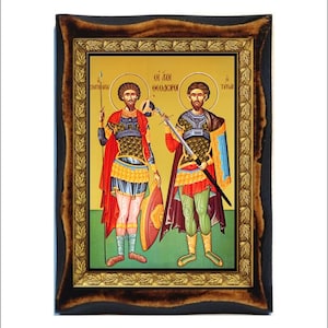 Pode incluir: Um ícone emoldurado que retrata dois santos, São Jorge e São Teodoro, em armaduras coloridas segurando espadas e escudos. O ícone tem um fundo dourado com uma moldura de folha de ouro e uma moldura de madeira escura.