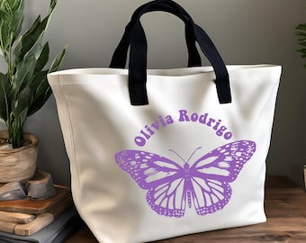 May include: White canvas tote bag with black handles. The bag has a purple butterfly graphic and the text "Olivia Rodrigo" in purple.