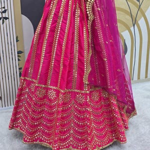 Pode incluir: Uma saia rosa com bordados dourados e trabalho de espelho. A saia tem uma dupatta rosa transparente com enfeites dourados.