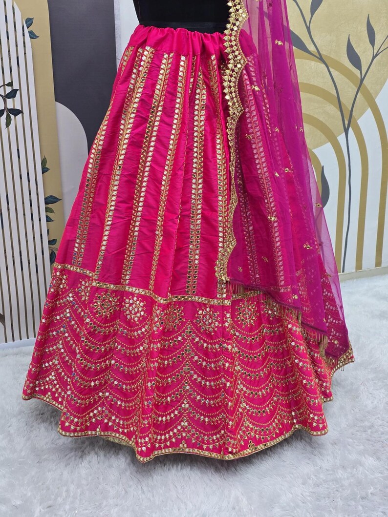 Pode incluir: Uma saia rosa com bordados dourados e trabalho de espelho. A saia tem uma dupatta rosa transparente com enfeites dourados.