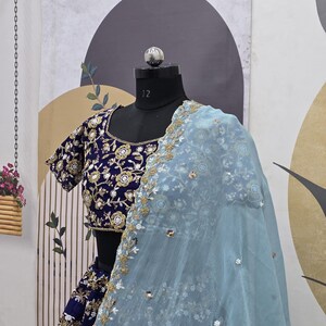 May include: A blue and gold embroidered bridal lehenga with a light blue sheer dupatta. The dupatta has a floral design and is decorated with sequins.