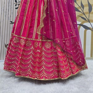 Pode incluir: Uma saia bordada em rosa e dourado com um dupatta transparente a condizer. A saia apresenta trabalhos de espelho intrincados e uma bainha festoneada.
