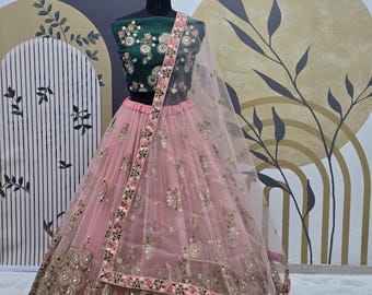 Può includere: Un completo lehenga choli ricamato rosa e verde. Il top verde scuro presenta ricami floreali, mentre la gonna rosa chiaro ha dettagli dorati e a specchio. Un dupatta rosa trasparente con ricami coordinati completa l'ensemble.