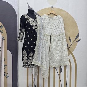 May include: A black and white embroidered dress with a white dupatta and matching palazzo pants. The dress has a V-neckline and long sleeves. The palazzo pants have a wide leg and are embellished with sequins.