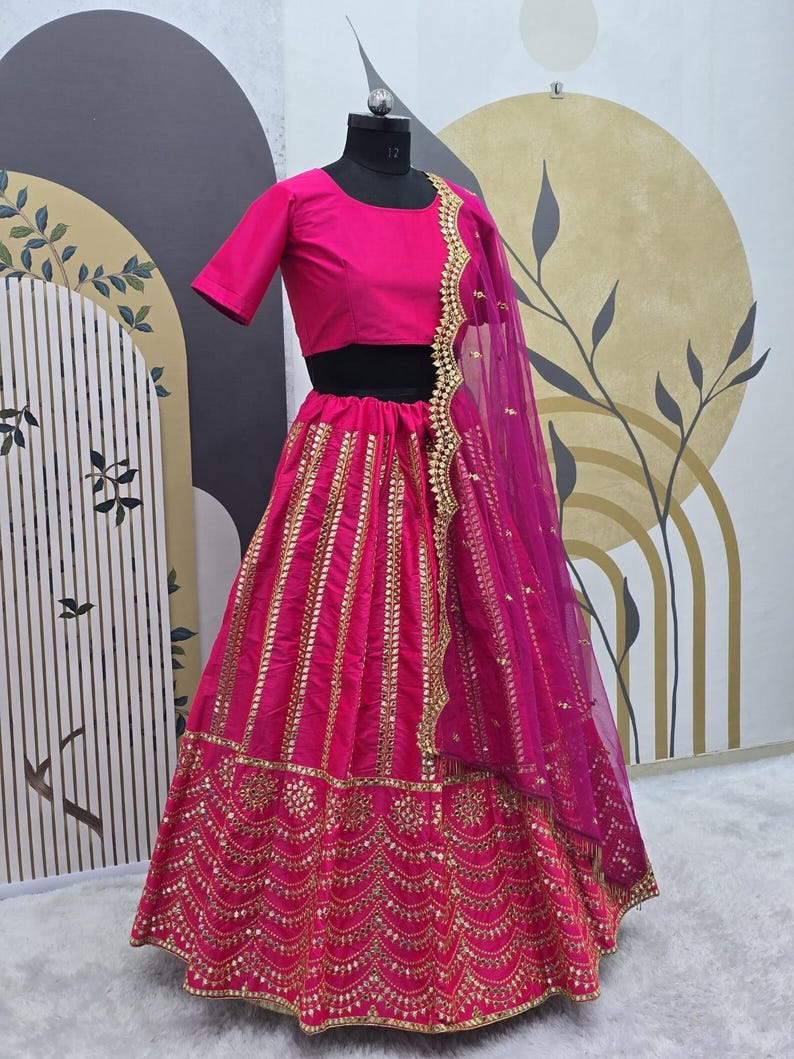 Pode incluir: Um lehenga bordado em rosa e dourado com um top curto rosa combinando. O lehenga tem uma saia em camadas com bordados dourados e lantejoulas. O dupatta &eacute; um tecido rosa transparente com bordados dourados.