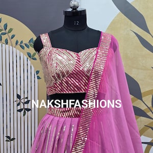 Op de afbeelding: Een roze en gouden sequined lehenga met een bijpassend topje. De outfit wordt getoond op een mannequin tegen een gepatroneerde achtergrond. De tekst "NAKSHFASHIONS" is zichtbaar op de rok.