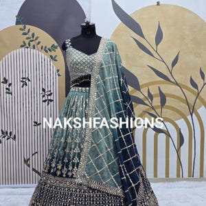 Puede incluir: Un lehenga bordado en azul verdoso y negro con un dupatta a juego. El lehenga tiene una falda de capas con un borde negro y adornos dorados. El dupatta es una tela transparente con un patrón a cuadros.
