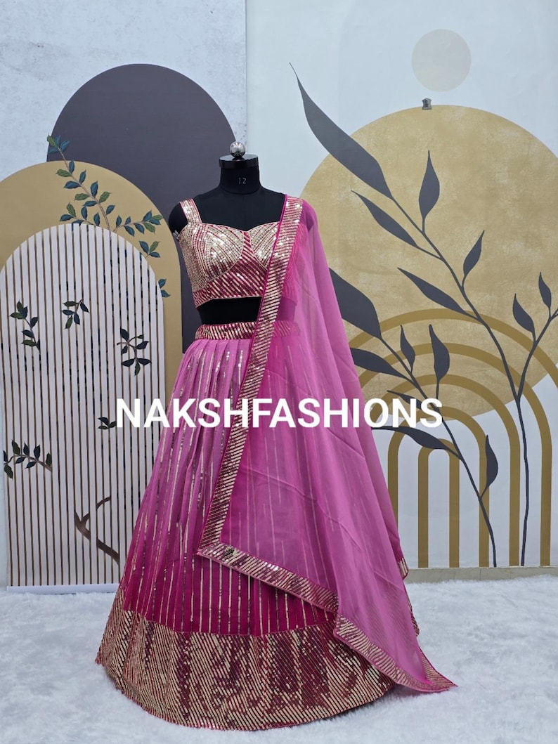 Op de afbeelding: Een roze en magenta lehenga met gouden pailletten en borduurwerk. De lehenga heeft een bijpassend topje en een doorschijnende roze dupatta.