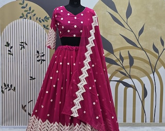 Puede incluir: Una falda larga magenta bordada con un top magenta a juego y una dupatta magenta transparente. La falda y el top tienen lunares blancos y la dupatta tiene un patrón de zigzag blanco.