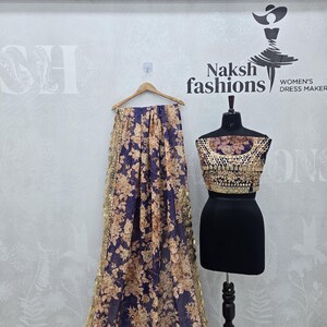 May include: A navy blue and gold floral patterned saree with a gold border is displayed on a wooden hanger. A black dress form displays a matching gold and brown embellished top and a black skirt. The text "Naksh fashions" is visible.