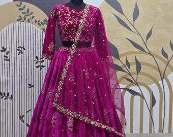Puede incluir: Un lehenga de terciopelo magenta con bordados y lentejuelas doradas. El lehenga tiene un top corto a juego con mangas largas. El atuendo es perfecto para una ocasión especial.