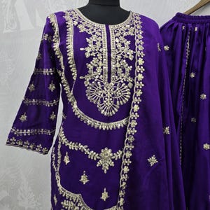 Peut inclure: Un ensemble en velours violet vif avec des broderies dor&eacute;es complexes. La tenue comprend une tunique &agrave; manches longues et un pantalon assorti, tous deux orn&eacute;s de motifs floraux et g&eacute;om&eacute;triques d&eacute;taill&eacute;s. La tunique est pr&eacute;sent&eacute;e sur un mannequin.