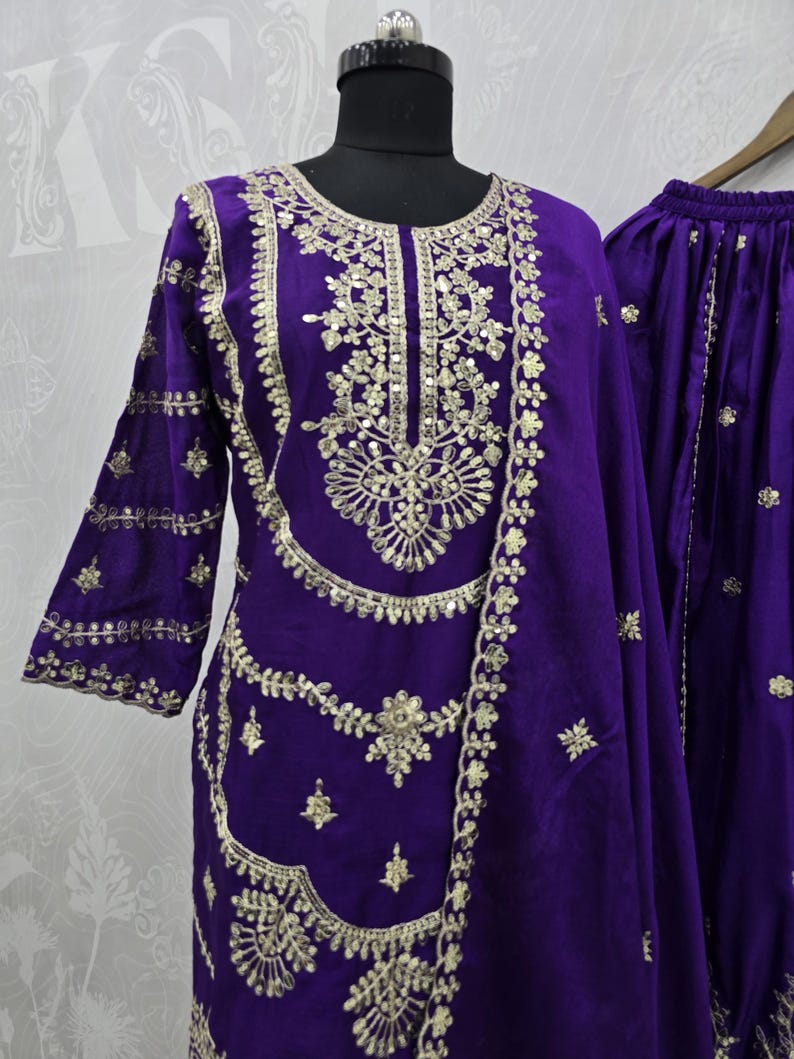 Peut inclure: Un ensemble en velours violet vif avec des broderies dor&eacute;es complexes. La tenue comprend une tunique &agrave; manches longues et un pantalon assorti, tous deux orn&eacute;s de motifs floraux et g&eacute;om&eacute;triques d&eacute;taill&eacute;s. La tunique est pr&eacute;sent&eacute;e sur un mannequin.