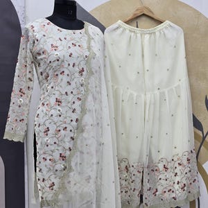 May include: A white embroidered salwar kameez set. The long-sleeved tunic and matching pants are adorned with floral embroidery and sequins. The set includes a sheer dupatta with a scalloped edge.