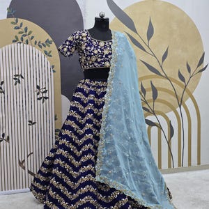 May include: A navy blue and gold embroidered lehenga with a zig-zag pattern. The lehenga is paired with a matching embroidered choli and a light blue sheer dupatta.