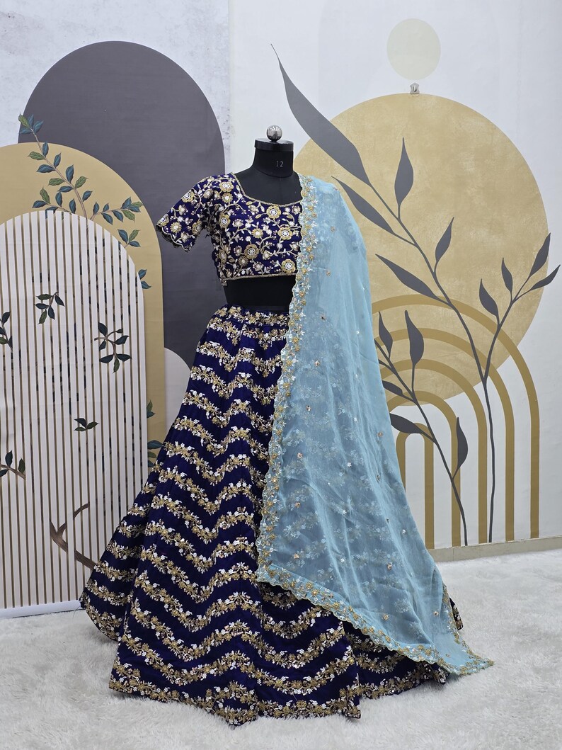 May include: A navy blue and gold embroidered lehenga with a zig-zag pattern. The lehenga is paired with a matching embroidered choli and a light blue sheer dupatta.