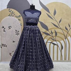 May include: A navy blue two-piece formal outfit. The top is a cropped, sleeveless design with silver embellishments. The skirt is a full, floor-length style with vertical stripes and scattered silver dots. The outfit is displayed on a mannequin.